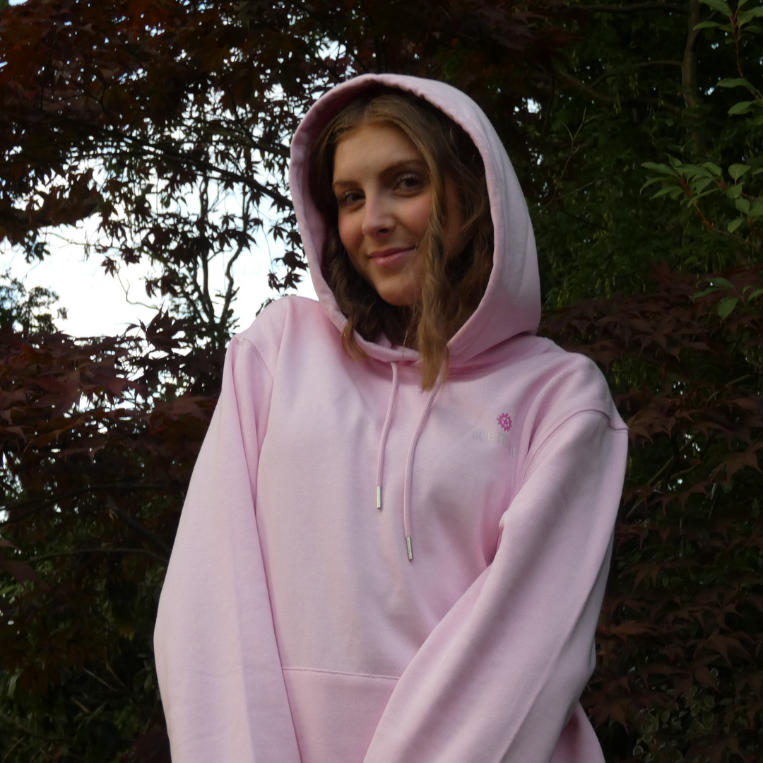 Person wearing a pink hoodie standing outdoors with trees in the background