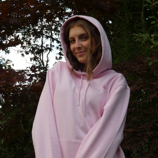 Person wearing a pink hoodie standing outdoors with trees in the background