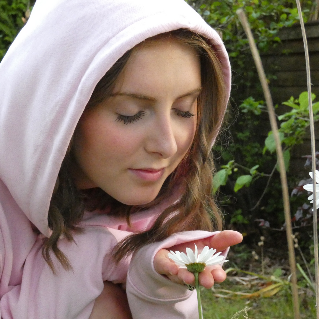 Person in pink hoodie holding a white flower in a garden setting