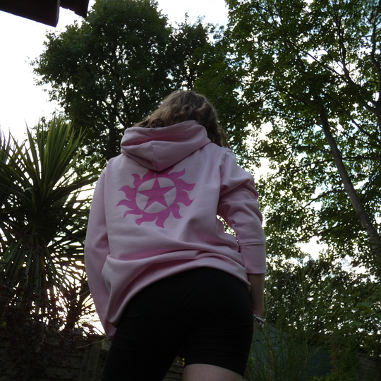 Person wearing a pink hoodie with a logo outdoors among trees