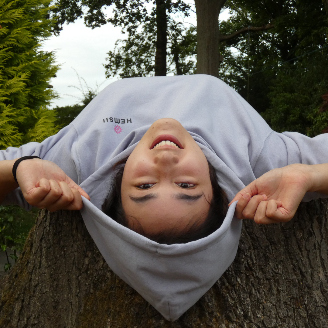 Person wearing a hoodie with text, standing on a tree stump outdoors.